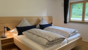 Een tweepersoonsbed met gestreepte beddengoed, een nachtkastje met lamp en een raam met gordijnen.