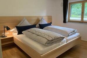 A double bed with striped bedding, a nightstand with a lamp, and a window with curtains. - Holiday apartment with 2 bedrooms (Oberstdorf)
