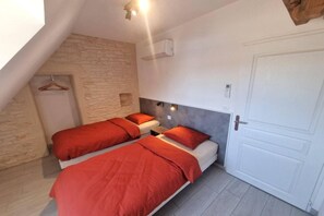 A bedroom with two beds, a stone wall, a white door, and a wooden ceiling beam. - Villa Rocamadour, Couzou (Couzou)