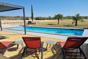 A swimming pool with a wooden deck, two red chairs, and a stone wall. - Villa Rocamadour, Couzou (Couzou)