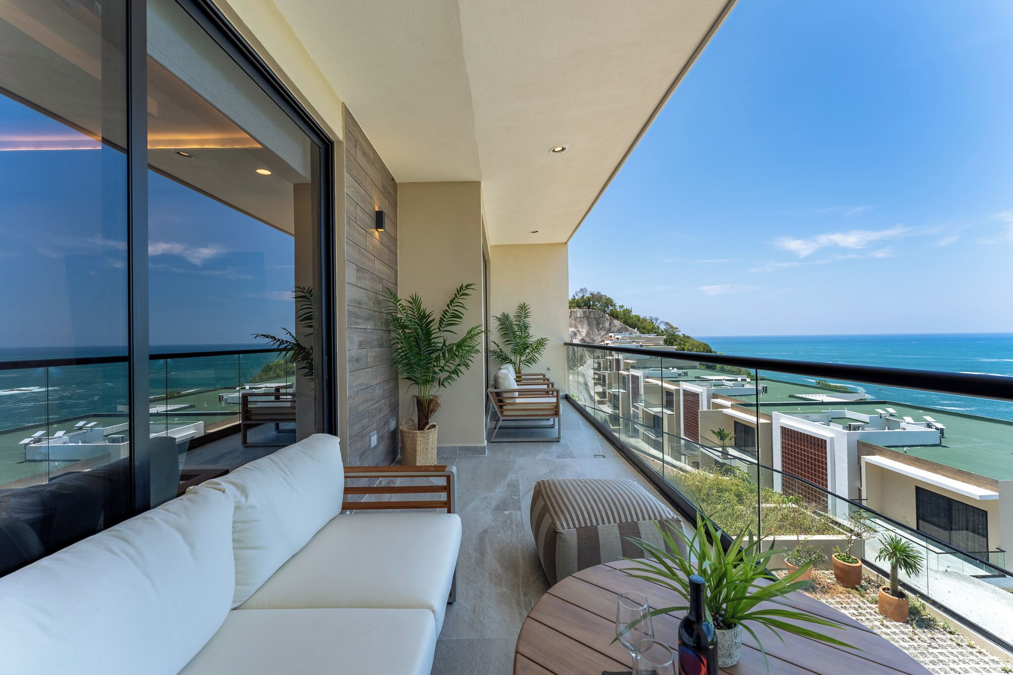 A balcony with a white sofa, potted plants, and a view of the ocean and buildings.