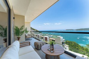 Ein Balkon mit Meerblick, eine Couch, ein runder Tisch mit Gläsern und Kübelpflanzen.