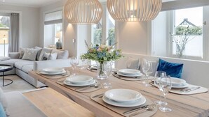 Spiseområde med et langt træbord dækket til et måltid, store vinduer og moderne indretning.