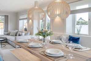 Comedor con una larga mesa de madera preparada para una comida, ventanas amplias y un diseño interior moderno.