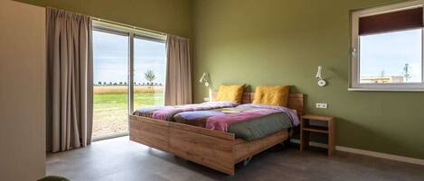 Un dormitorio con cama de madera, una mesita de noche pequeña, una silla y un ventanal con cortinas.