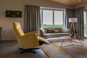 A modern living room with a sofa, armchair, and coffee table, large windows with curtains, and a floor lamp. - Holiday home in Zonnemaire with Wi-Fi (Zonnemaire)
