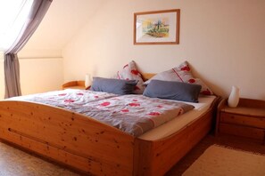 Una cama individual con estructura de madera, dos almohadas, una mesita de noche y un cuadro en la pared.