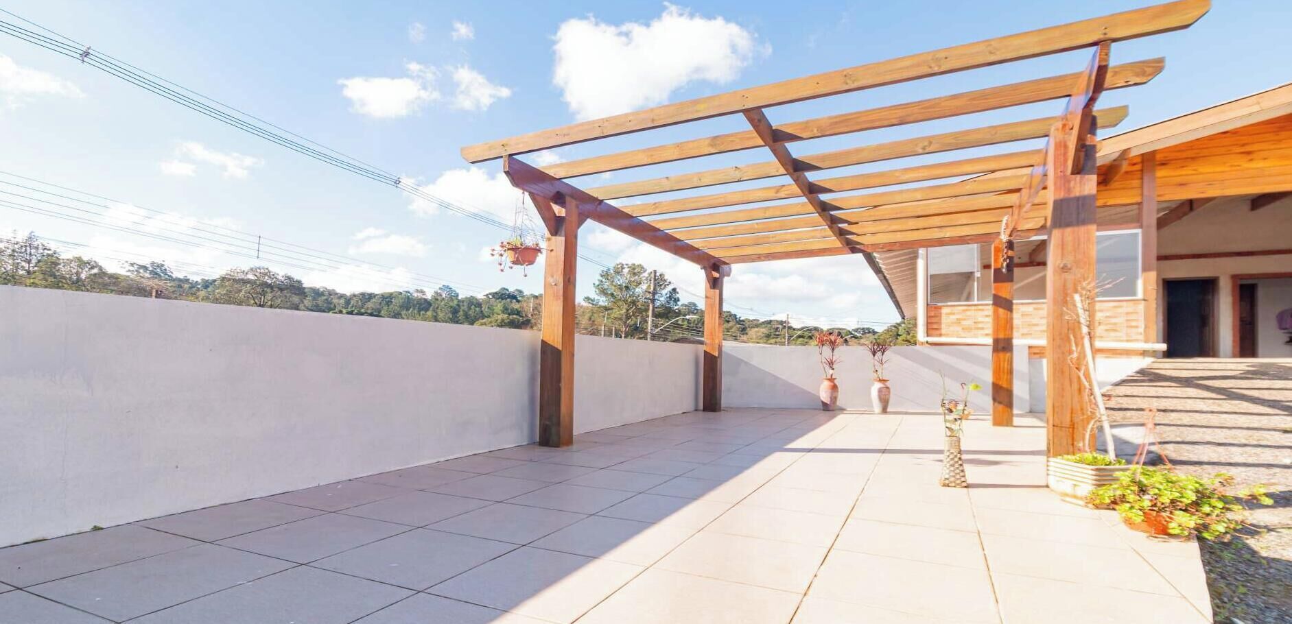 A covered outdoor area with a pergola structure, tiled flooring, and potted plants.