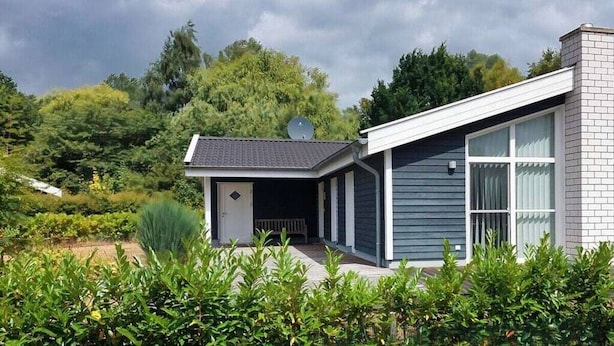 Une maison moderne dotée d’un porche abrité, d’une antenne parabolique et d’un jardin en premier plan.