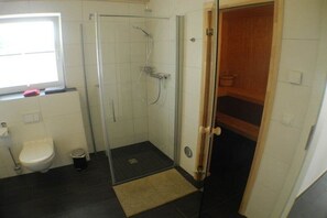 Een badkamer met toilet, douchecabine en een houten deur.