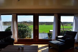 A room with a large window offering a view of a green field and trees. There are two chairs and a table in the room. - Holiday home in Bad Bentheim with Wi-Fi (Bad Bentheim)