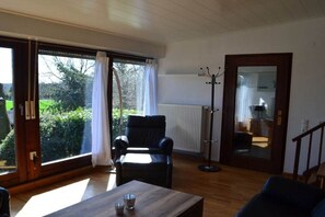 A room with a large window, a black leather chair, a wooden table, and a floor lamp. - Holiday home in Bad Bentheim with Wi-Fi (Bad Bentheim)