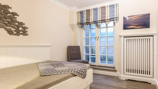 Un dormitorio con cama, ventana con vistas, radiador y un adorno en la pared.