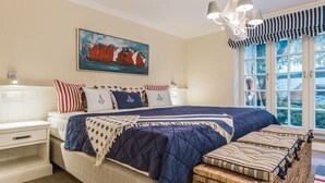 Quarto com cama grande, mesa de cabeceira, luminária, quadro e janela com cortinas.