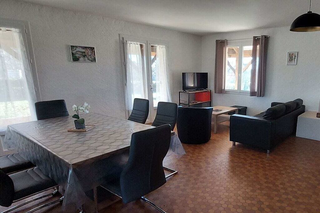 A living room with a dining table, chairs, a sofa, a TV, and a window with curtains.