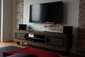 Ein modernes Wohnzimmer mit Flachbildfernseher an einer Steinwand, einer Holz-Unterhaltungsecke und einem roten Teppich auf dem Boden.