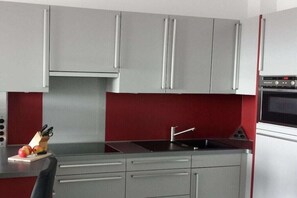 Eine Küche mit grauen Schränken, einer roten Spritzschutzwand und einem eingebauten Backofen.