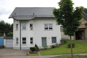 A two-story residential building with a tiled roof, multiple windows, and a small front yard with a tree. - Holiday apartment Rhine-Ahr (Sinzig)
