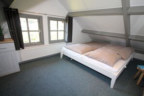 Ein Schlafzimmer mit Etagenbett, zwei mit Vorhängen versehenen Fenstern, einem Heizkörper, einem kleinen Tisch und einer Topfpflanze.