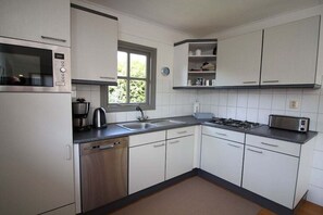 Una cocina con armarios blancos, lavavajillas, microondas, tostadora y ventana.