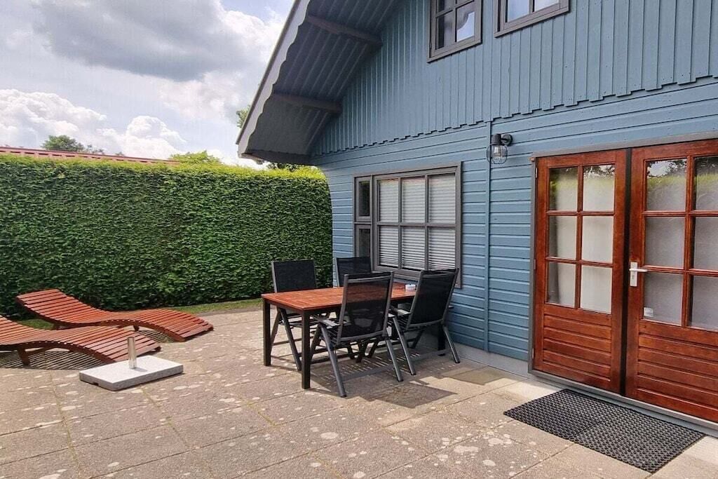Une maison bleue avec un patio comprenant une table et des chaises, une porte en bois et une haie.