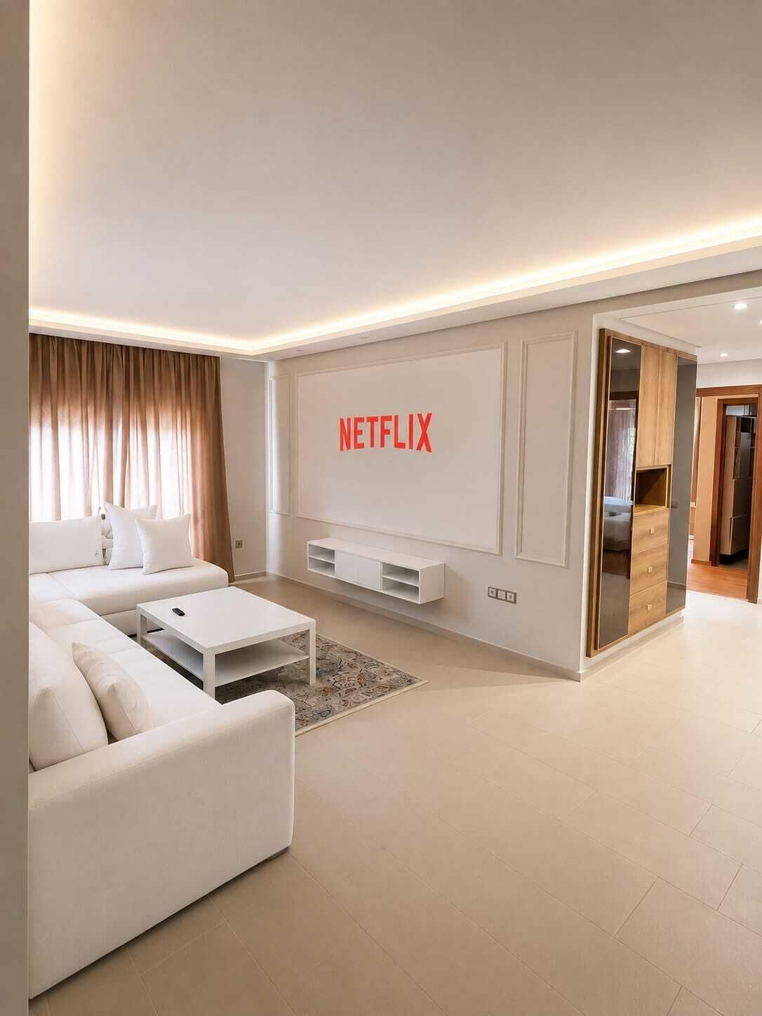 Un saló modern amb un sofà blanc, una taula de centre i un televisor fixat a la paret amb el logotip de Netflix.