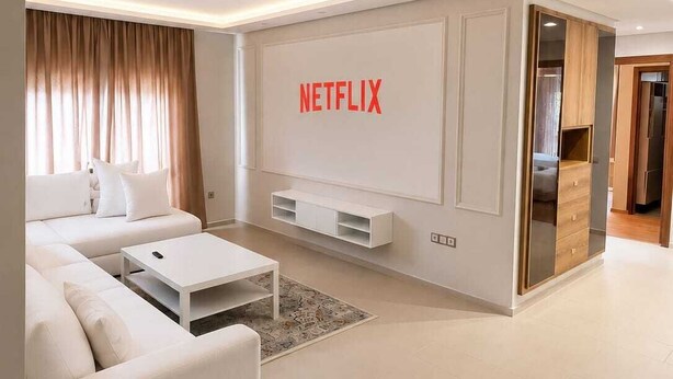 Un soggiorno moderno con un divano bianco, un tavolino da caffè e un televisore a parete con il logo Netflix.