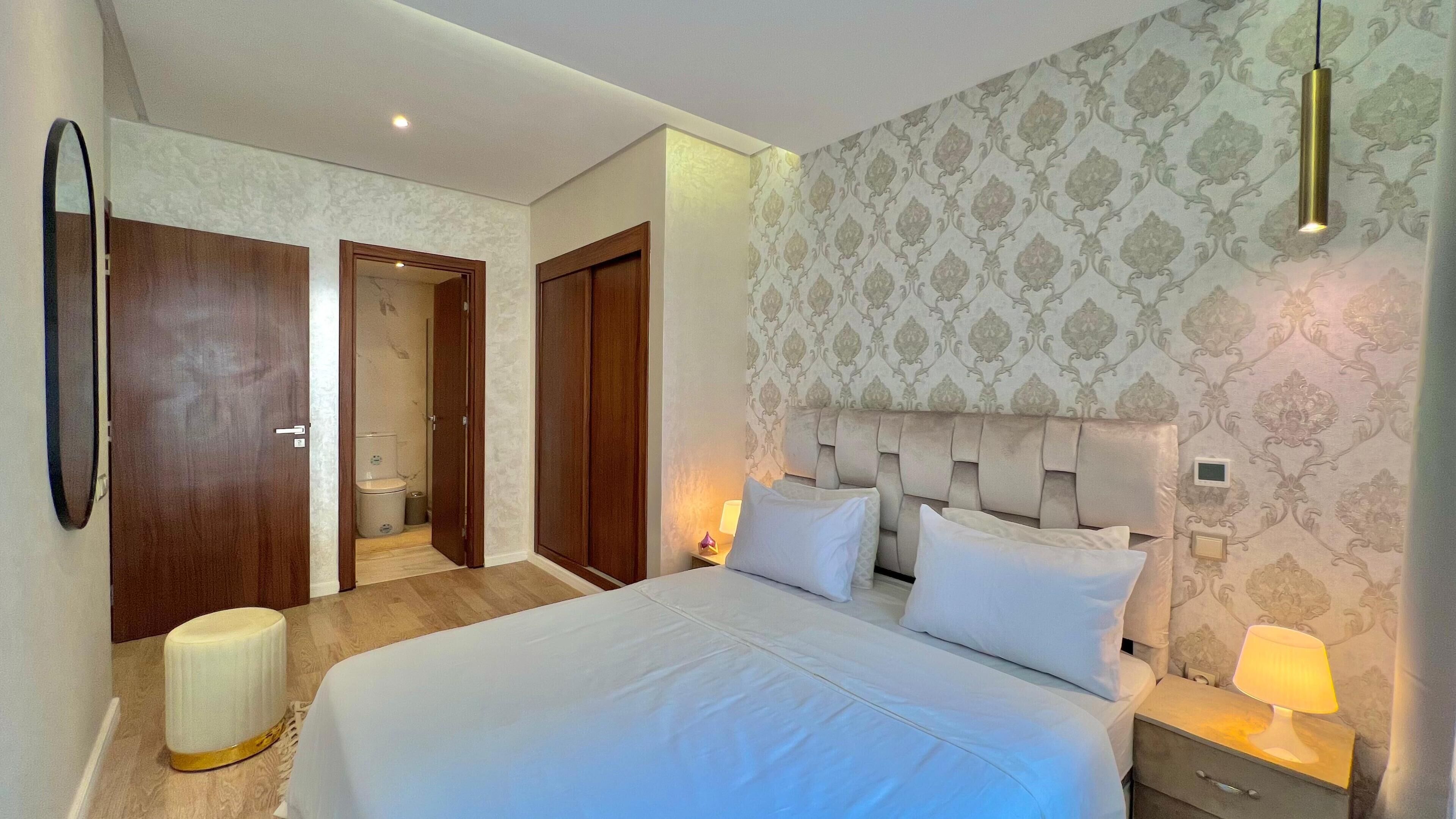 Habitació d'hotel amb llit, taula de nit, làmpada i bany amb vàter i dutxa.