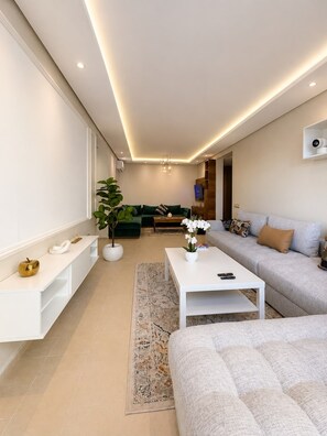 Un salon moderne avec un canapé blanc, une table basse et, au fond, un canapé vert.