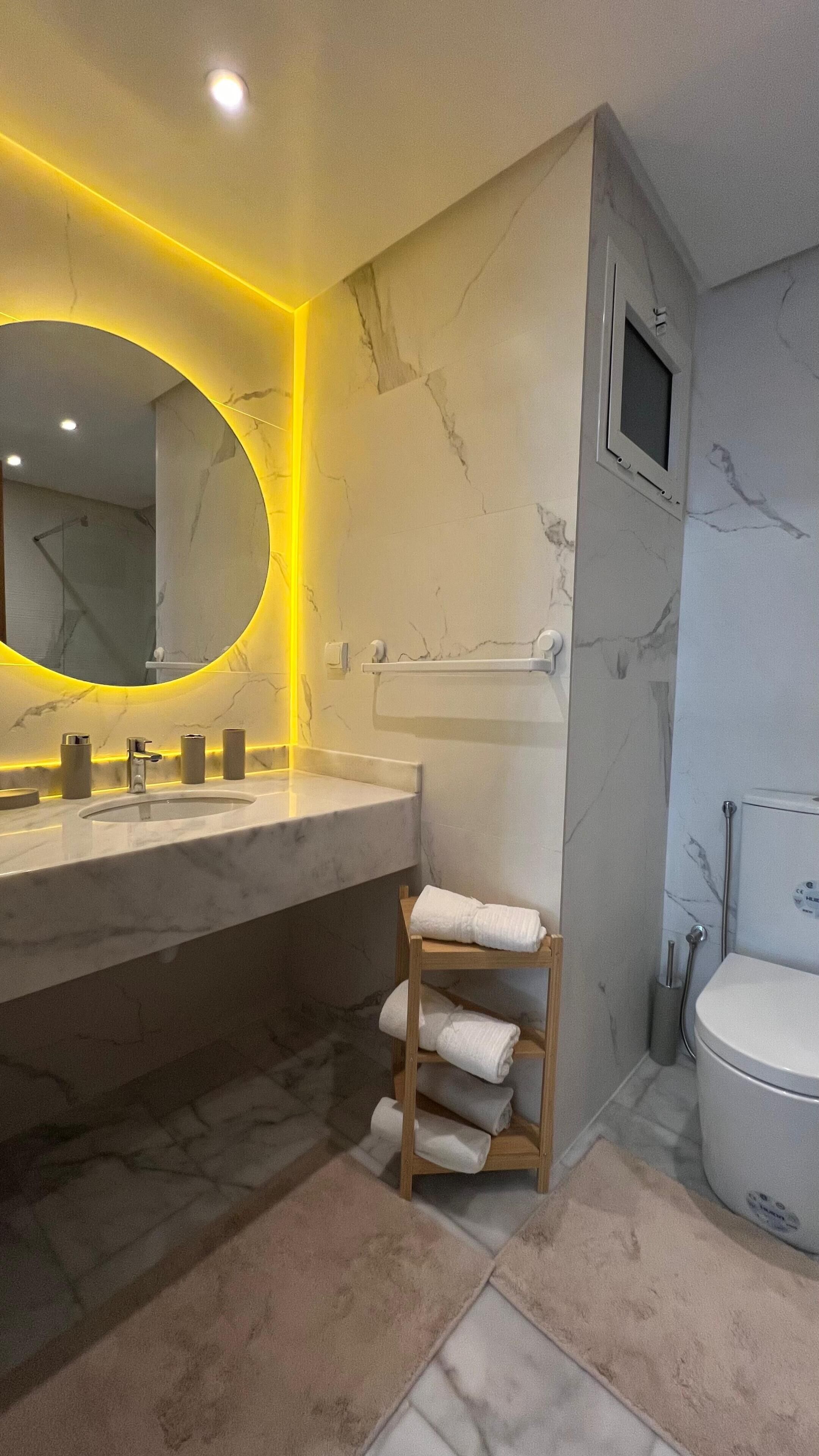Un bany modern amb un lavabo de marbre, un suport per tovalloles de fusta i un vàter.