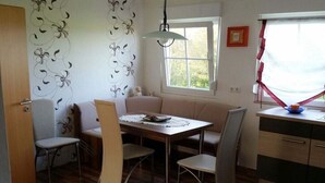 Un comedor con mesa, sillas, banco, ventana con cortinas y pared con estampado floral.