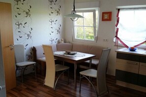 Een eethoek met een tafel, stoelen, een bank, een raam met gordijnen en een muur met bloemenbehang.