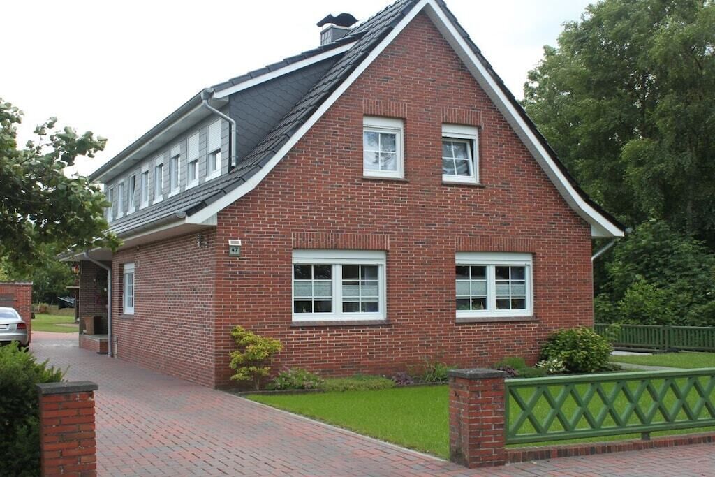 Et toetages murhus med saddeltag, en veranda og et grønt hegn.