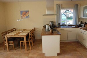 A compact kitchen with a dining table, chairs, a coffee maker, and a window with a view of a house. - Holiday home with 1 bedroom (Seebad Heringsdorf)