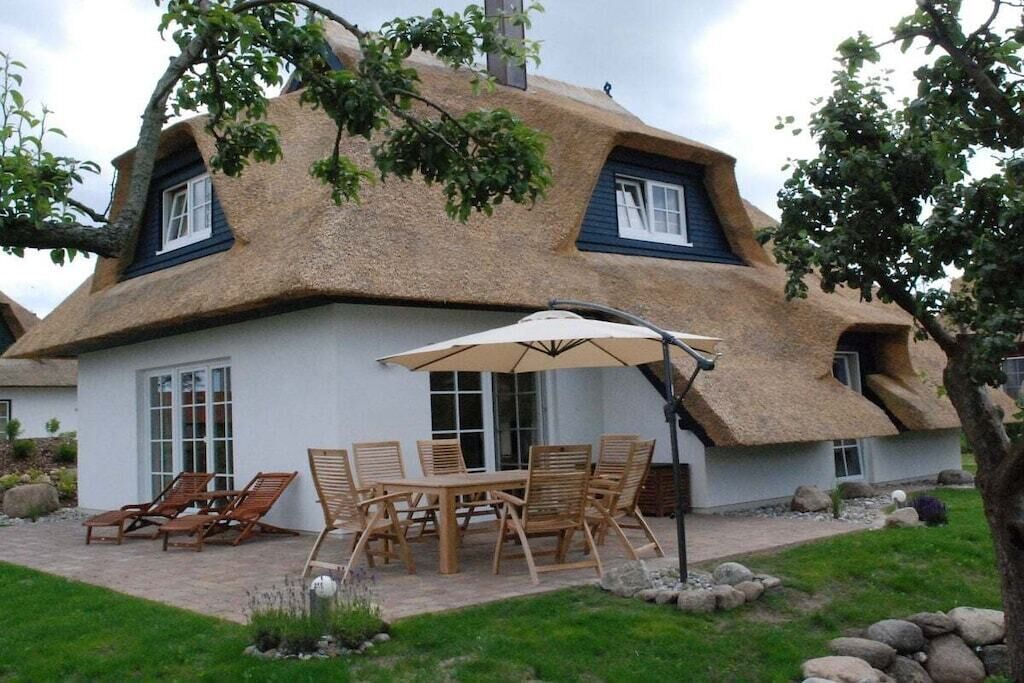 A thatched-roof house with a patio area, outdoor furniture, and a large umbrella.