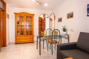 A living room with a wooden cabinet, a green metal chair, a grey sofa, and a small table with a plant. - Holiday apartment with 1 bedroom (Costa Calma)