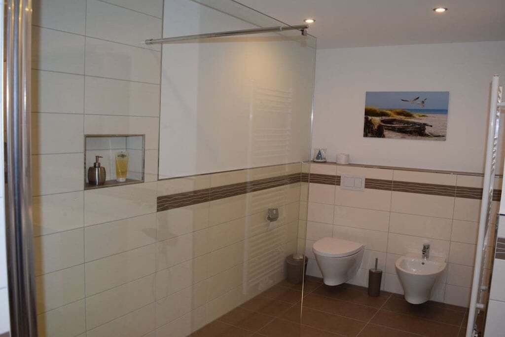 Een badkamer met een douchecabine van glas, een toilet, een bidet en een klein plankje met toiletartikelen.