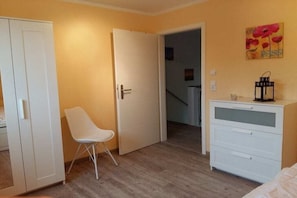 A room with a white wardrobe, a white chair, a white dresser, and a door leading to another room. - Holiday home with 4 bedrooms (Ostseebad Rerik)