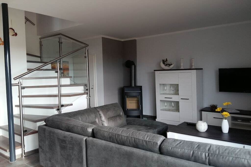 A modern living room with a grey sofa, a fireplace, a TV, and a staircase.