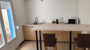 Et moderne køkken med en central ø, træstole, en hængende pendel og et vindue med persienner.