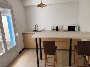 A modern kitchen with a central island, wooden chairs, a hanging pendant light, and a window with blinds. - 3-bedroom family home with parking, perfect for exploring Arras and the surrounding area (Anzin-Saint-Aubin)