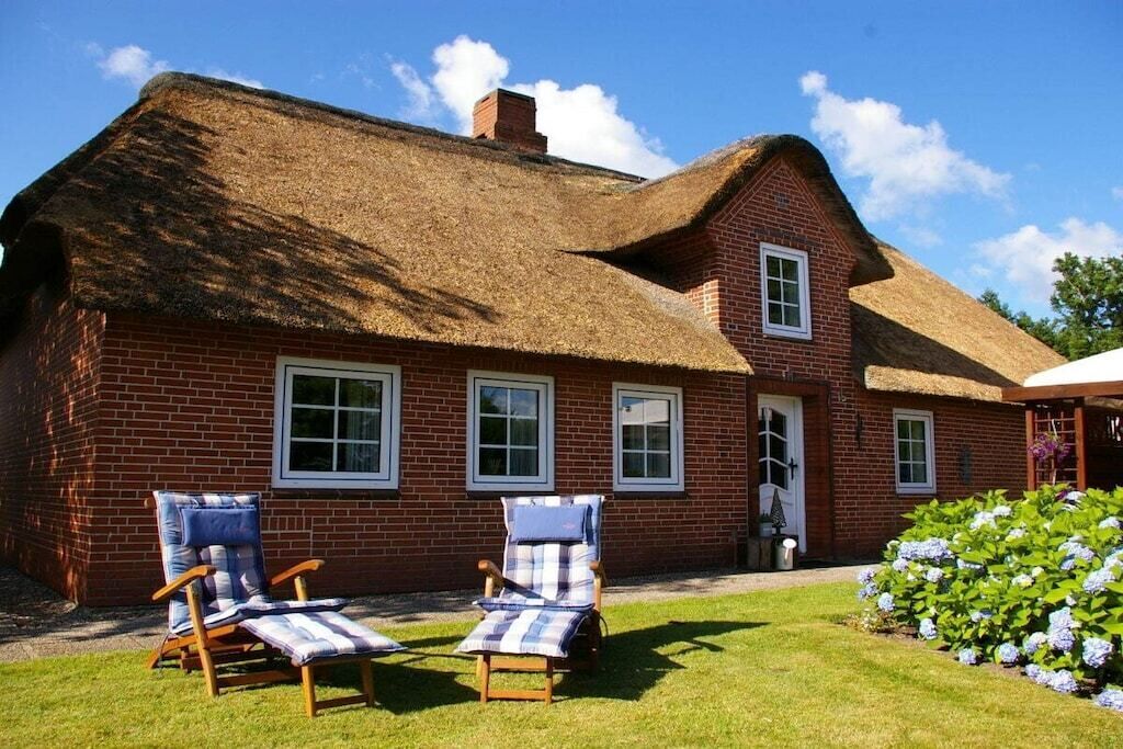 A brick house with a thatched roof, two lounge chairs with striped cushions, and a well-maintained lawn.