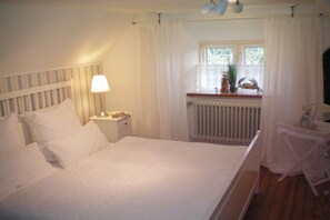 Una camera da letto con un letto, un comodino, una lampada, una finestra con tende e un termosifone.