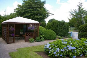 Un gazebo in legno con tetto bianco, immerso in un giardino con cespugli di ortensie.