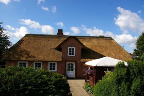 Una casa tradizionale in mattoni con tetto di paglia, un portone e un piccolo portico con un ombrello bianco.