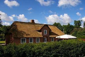 Une maison traditionnelle en briques, avec un toit de chaume, entourée de verdure.
