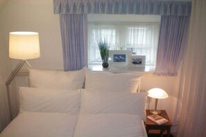 A hotel room with a bed, two bedside lamps, a nightstand with a book, and a window with curtains. - Holiday home with 4 bedrooms (Risum-Lindholm)
