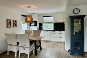 Een moderne keuken met witte kastjes, een eettafel met stoelen en een klok aan de muur.