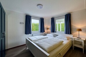 Een slaapkamer met een tweepersoonsbed, twee nachtkastjes en een raam met gordijnen.