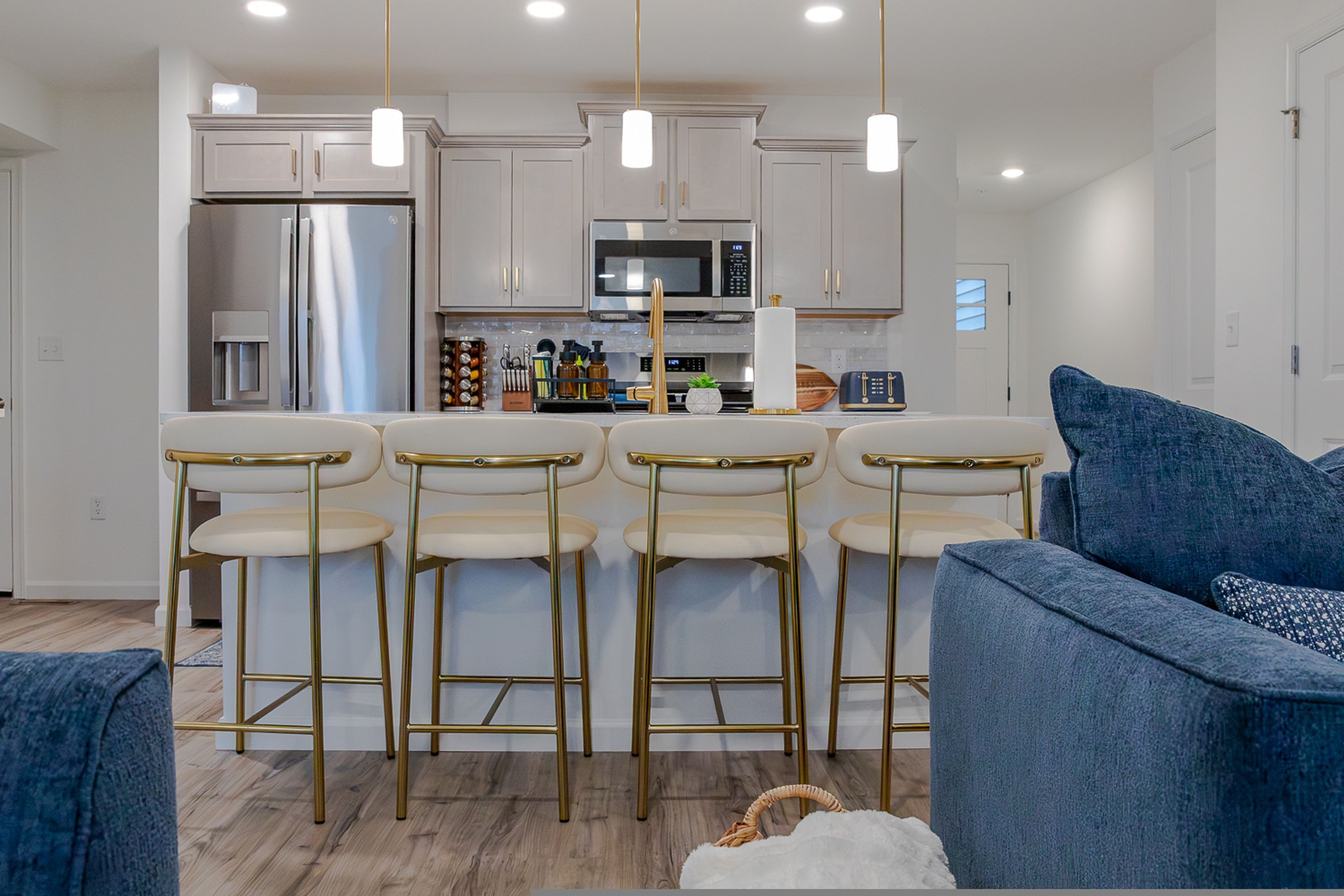 A modern kitchen with stainless steel appliances, a central island with bar stools, and a blue sofa in the foreground.